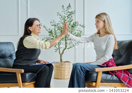 Smiling female psychologist giving high five to teenage girl at therapy Smiling female psychologist giving high five to teenage girl at therapy 141053224