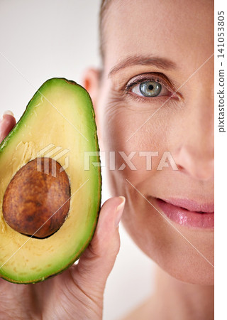 Skincare, avocado and closeup face of woman in studio for health, wellness or natural facial routine. Smile, beauty and mature person with organic fruit for dermatology treatment by white background. Skincare, avocado and closeup face of woman in studio for health, wellness or natural facial routine. Smile, beauty and mature person with organic fruit for dermatology treatment by white background. 141053805
