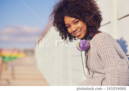 Woman, smile and portrait in city for travel, walk and break in urban for summer, fun and outdoor. African person and happy with headphones for music, streetwear and journey in town for trip 141054068