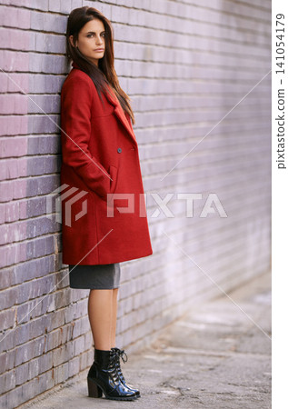 Winter, fashion and woman on wall with jacket in city and travel with cool style in red coat. Streetwear, clothes and girl outdoor on building background with confidence and pride in New York morning Winter, fashion and woman on wall with jacket in city and travel with cool style in red coat. Streetwear, clothes and girl outdoor on building background with confidence and pride in New York morning 141054179