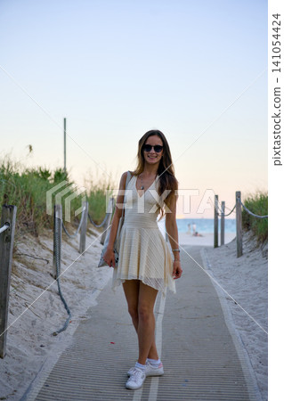 Stylish Woman Walking on Wooden Boardwalk to Beach at Sunset Stylish Woman Walking on Wooden Boardwalk to Beach at Sunset 141054424