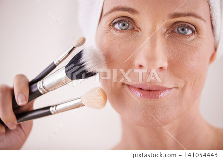 Brush, makeup and mature woman in portrait or studio for cosmetics, beauty and facial treatment. Smile, face or model with foundation, tools or powder in skincare routine on white background for glow Brush, makeup and mature woman in portrait or studio for cosmetics, beauty and facial treatment. Smile, face or model with foundation, tools or powder in skincare routine on white background for glow 141054443