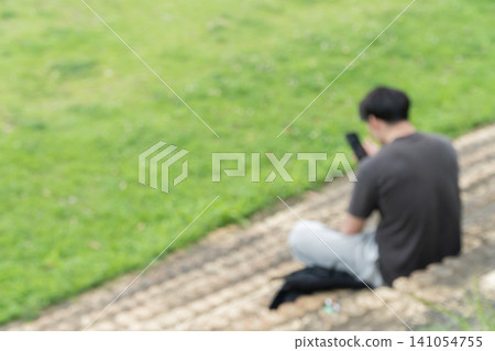 A young man is sitting on the steps of a park looking at his smartphone. A young man is sitting on the steps of a park looking at his smartphone. 141054755