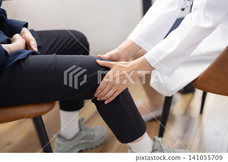 一位女醫生正在檢查病人膝蓋，鏡頭特寫她的雙手。 141055709