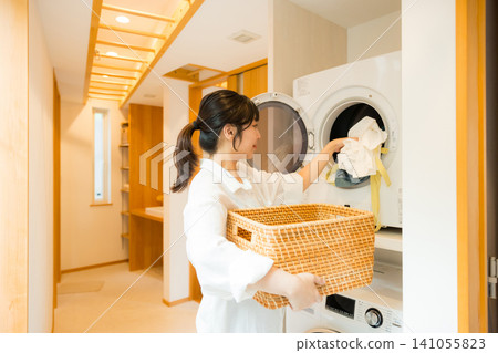 一位女士正在從烘乾機裡取出衣物。 一位女士正在從烘乾機裡取出衣物。 141055823