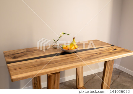 A wooden table displays a bowl of fruit and a small vase with a flower in a clean indoor space. The table stands firmly with sturdy legs A wooden table displays a bowl of fruit and a small vase with a flower in a clean indoor space. The table stands firmly with sturdy legs 141056053