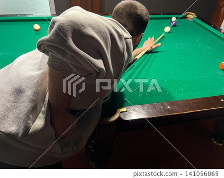 A player focuses on making a shot in a game of pool while standing close to the table. Friends can be seen in the background A player focuses on making a shot in a game of pool while standing close to the table. Friends can be seen in the background 141056065