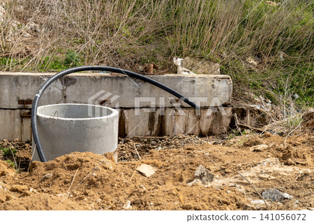 A construction site has a round concrete structure and a black pipe placed on dirt. Grass and plants grow around the area 141056072