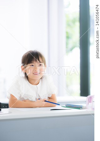 A kindergarten or elementary school girl concentrating on studying while looking at the blackboard in the classroom; studying for exams or other learning activities. 141056474