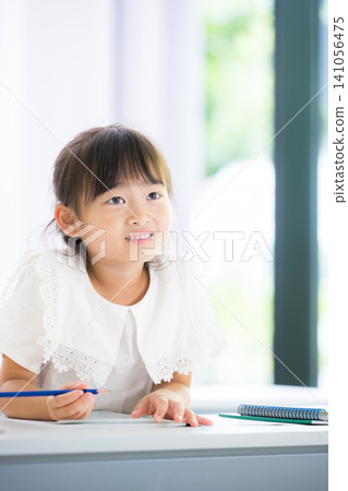 A kindergarten or elementary school-aged girl concentrating on studying while looking at the blackboard in a classroom; an image that evokes images of cram school, regular school, exams, and studying. 141056475