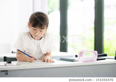 A kindergarten or elementary school-aged girl concentrating on math drills in a classroom; an image of a cram school, regular school, exams, studying, and learning. 141056476