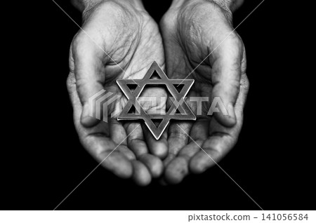 Jewish star of david in mature man hands over black background. Holocaust Remembrance Day Jewish star of david in mature man hands over black background. Holocaust Remembrance Day 141056584