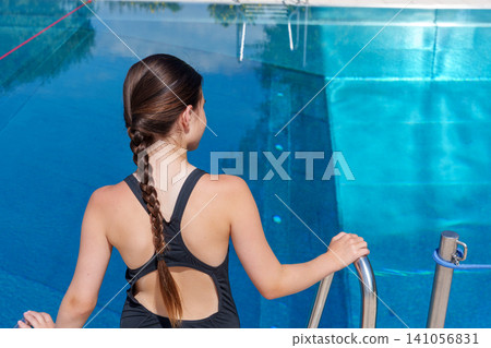 Teen girl entering swimming pool by metal ladder 141056831