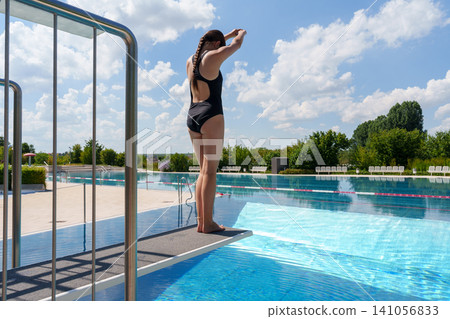 Teen girl preparing to jump from diving board at pool Teen girl preparing to jump from diving board at pool 141056833