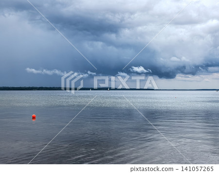 Dramatic storm clouds over a calm lake with orange buoy and sailboats Dramatic storm clouds over a calm lake with orange buoy and sailboats 141057265