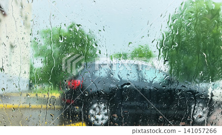 Raindrops streaming down car window with blurred vehicles and trees behind Raindrops streaming down car window with blurred vehicles and trees behind 141057266