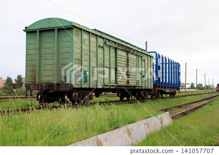 Freight cars on railroad tracks. Green freight car is coupled to an empty blue flatcar for transporting timber Freight cars on railroad tracks. Green freight car is coupled to an empty blue flatcar for transporting timber 141057707