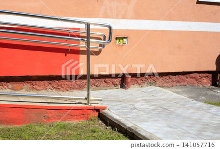 Disabled call button assistance system near an accessible wheelchair ramp. Yellow handicap symbol sign sits on a textured concrete wall Disabled call button assistance system near an accessible wheelchair ramp. Yellow handicap symbol sign sits on a textured concrete wall 141057716