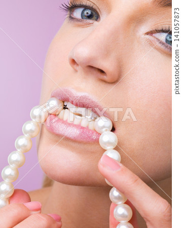 Woman, studio and bite pearl necklace in portrait for beauty, cosmetic or closeup by purple background. Girl, person and model with jewelry for wellness with facial skincare, makeup or transformation 141057873