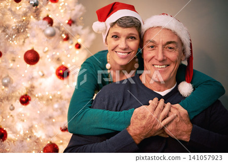 Christmas, portrait and senior couple with love, care and support together in a home on holiday. Tree, retirement and marriage with a smile and hug in a house with celebration and santa hat with joy 141057923
