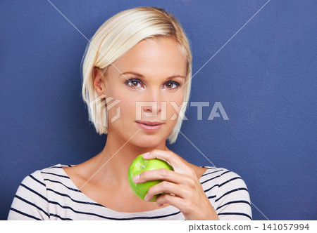 Woman, portrait and apple in studio for nutrition diet on blue background or fruit vitamin, snack or fibre. Female person, relax and wellness eating or mockup space as vegan detox, raw or lose weight Woman, portrait and apple in studio for nutrition diet on blue background or fruit vitamin, snack or fibre. Female person, relax and wellness eating or mockup space as vegan detox, raw or lose weight 141057994