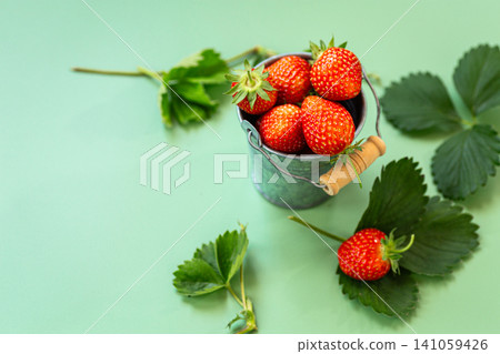 Fresh strawberries spilling from metal bucket on green background Fresh strawberries spilling from metal bucket on green background 141059426