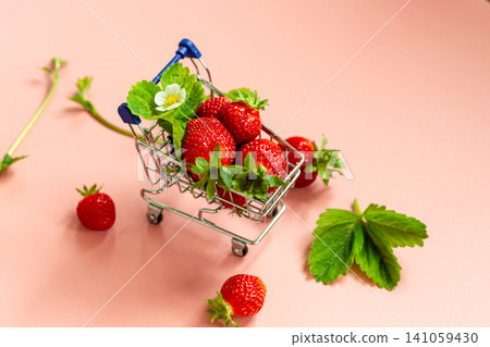 Red strawberries and green leaves in miniature cart on soft pink background Red strawberries and green leaves in miniature cart on soft pink background 141059430