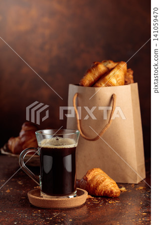 Black coffee and paper bag with croissants. Black coffee and paper bag with croissants. 141059470