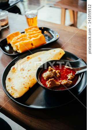Indian Chicken Curry with Roti Flatbread and Toasted Bread on Wooden Table Indian Chicken Curry with Roti Flatbread and Toasted Bread on Wooden Table 141059512