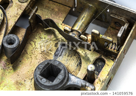 Detailed macro photograph of an old vintage brass door lock mechanism revealing intricate internal components including worn metal levers springs square spindle socket and aged patina surfaces 141059576