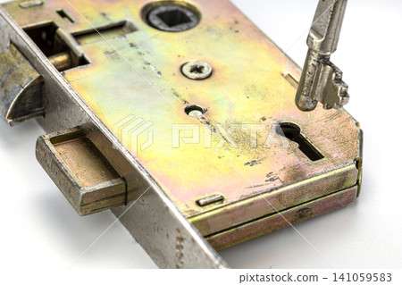 Detailed macro close up view of an old brass mortise door lock mechanism with a metal skeleton key inserted into the keyhole showing bolt latch screw and worn scratched golden yellow metal surface 141059583