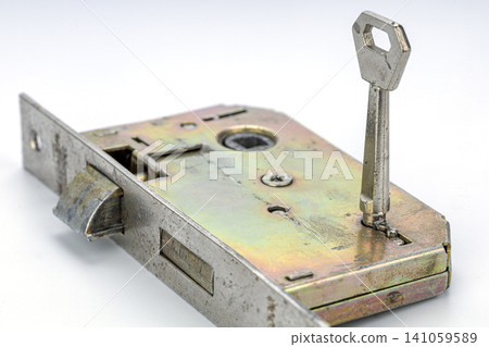 Close-up View of an Antique Metallic Mortise Door Lock Mechanism with a Nickel Plated Key Inserted into the Keyhole Showing Latch Bolt and Internal Components on White Background Close-up View of an Antique Metallic Mortise Door Lock Mechanism with a Nickel Plated Key Inserted into the Keyhole Showing Latch Bolt and Internal Components on White Background 141059589