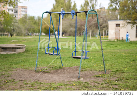 Old playground swing stands on green lawn in city park. Old playground swing stands on green lawn in city park. 141059722