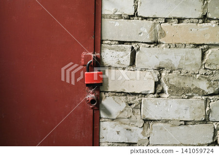 Red padlock hangs locked on metal door near old brick wall. Red padlock hangs locked on metal door near old brick wall. 141059724