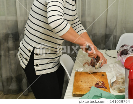 Adult woman cleaning salty herring fish on wooden board. Adult woman cleaning salty herring fish on wooden board. 141059764