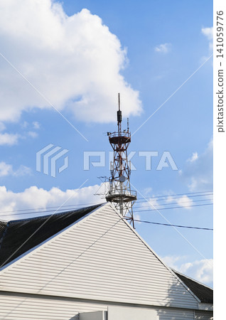 antenna rising behind house roof with triangular facade against blue sky antenna rising behind house roof with triangular facade against blue sky 141059776