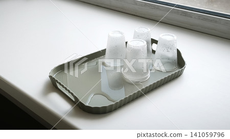 cups arranged upside down on tray filled with water on white windowsill by window. cups arranged upside down on tray filled with water on white windowsill by window. 141059796