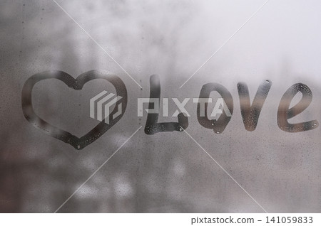 Heart shape and love word drawn on wet glass window pane covered with condensation water drops. Heart shape and love word drawn on wet glass window pane covered with condensation water drops. 141059833