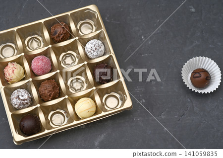 Chocolate assortment presented in square golden box on dark surface. Chocolate assortment presented in square golden box on dark surface. 141059835