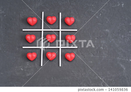Chocolate hearts filling entire tic tac toe grid on dark stone background. Chocolate hearts filling entire tic tac toe grid on dark stone background. 141059836