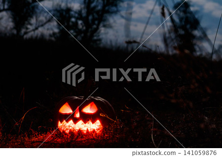 Spooky Halloween pumpkin jack-o-lantern with burning candles in scary forest at night 141059876