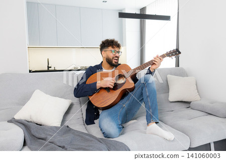 Happy man playing acoustic guitar on sofa Happy man playing acoustic guitar on sofa 141060003