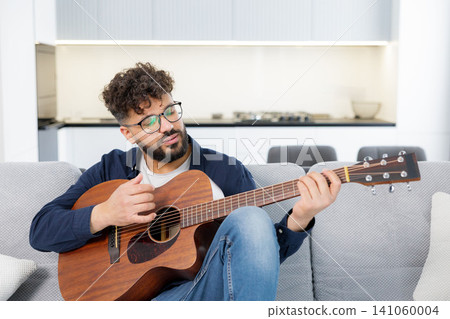 Man playing acoustic guitar and singing on sofa 141060004