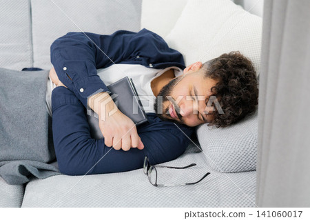 Man napping on sofa holding book at home Man napping on sofa holding book at home 141060017