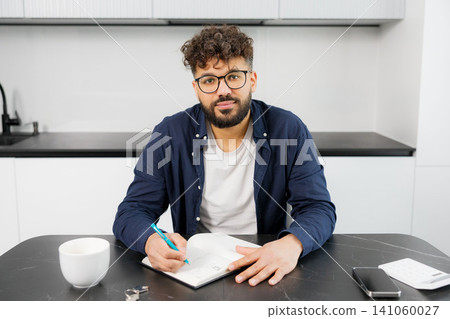 Young man planning personal finances at home kitchen Young man planning personal finances at home kitchen 141060027
