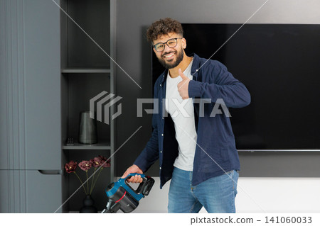 Man cleaning living room with cordless vacuum giving thumbs up Man cleaning living room with cordless vacuum giving thumbs up 141060033