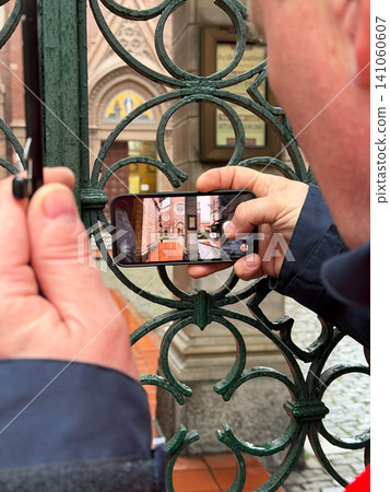 Tourist photographs historic building through ornamental iron gate with smartphone in Istanbul. Travel, tourism, mobile photography, cultural heritage, architecture, sightseeing, city exploration 141060607