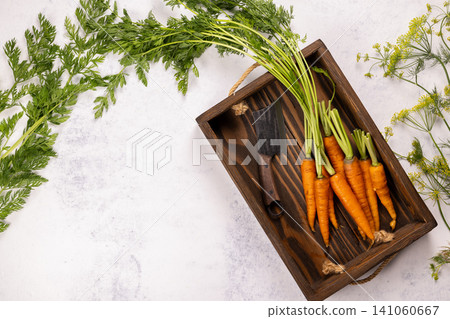 Fresh baby carrots with green tops and a cleaver on wooden tray Fresh baby carrots with green tops and a cleaver on wooden tray 141060667