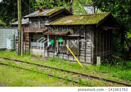 An old wooden hut with a moss-covered roof stands beside the railway tracks, amidst a landscape of fresh greenery. An old wooden hut with a moss-covered roof stands beside the railway tracks, amidst a landscape of fresh greenery. 141061762