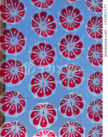 Vibrant red floral umbrellas suspended over a street in Agueda Portugal forming a beautiful and festive canopy art installation under the summer sky 141062177
